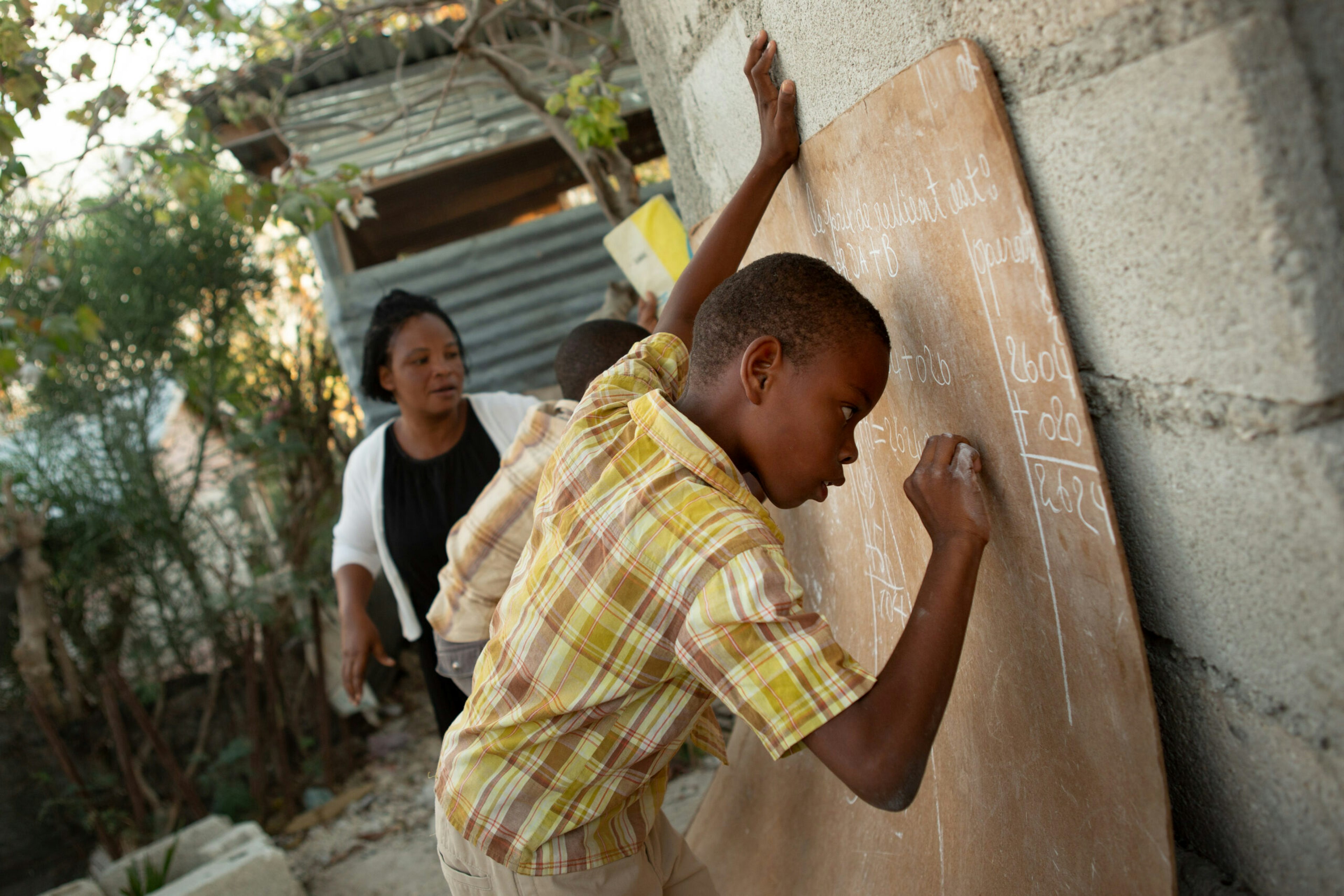 Elvige Edrice’s children, Baron Ritcharmant, 9, right, and his brother, Céléstin Shneïder, 7, puzzle out their math homework in chalk in the backyard of the family’s home in Canaan, Haiti, Jan. 8, 2019.